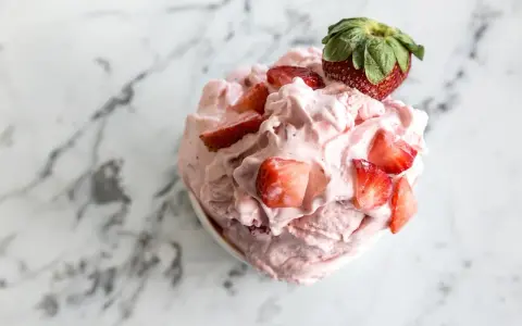 Un délice rose et crémeux : un sorbet fraise garni de morceaux de fruits frais et d'une fraise entière sur un fond marbré.