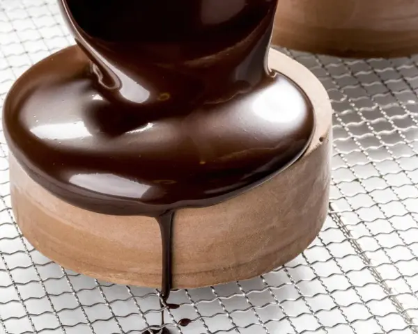 Un glaçage chocolat brillant et onctueux recouvre un petit gâteau rond, coulant sur les côtés.