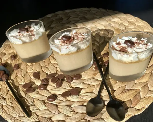 Trois verrines de crème au café facile, garnies de chantilly, cacao et grains de café. Des chocolats en forme de grains parsèment le napperon.