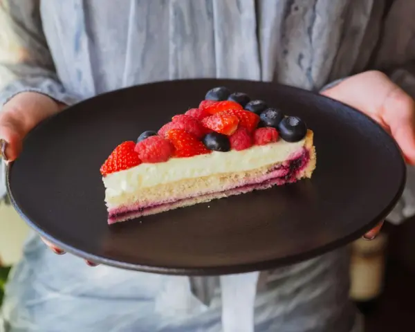Tranche de tarte aux fruits rouges sur une crème mousseline onctueuse, présentée sur une assiette noire.