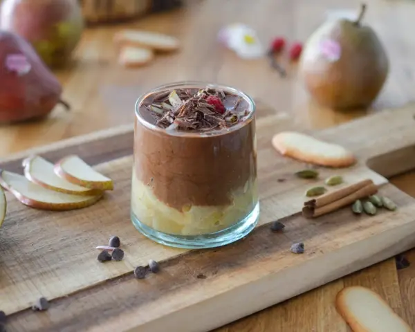 Délicieuse recette mousse poire chocolat, garnie de copeaux de chocolat et d'une framboise. Poires fraîches et épices sur fond de bois.