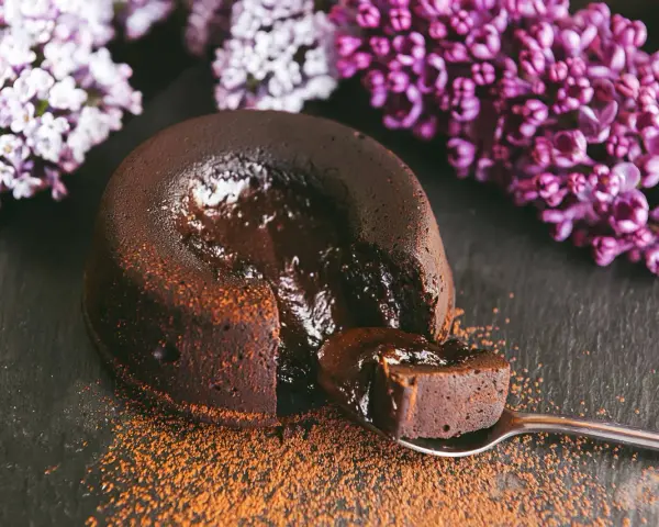 Un fondant au chocolat coulant, saupoudré de cacao, avec des fleurs de lilas en arrière-plan. Une bouchée parfaite.