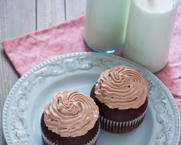 Deux cupcakes au chocolat avec une ganache chocolat passion onctueuse, servis sur une assiette bleue avec deux verres de lait.