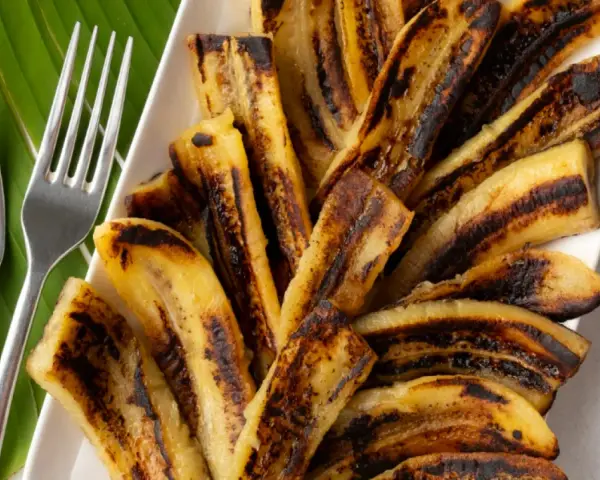 Bananes flambées grillées sur une feuille de bananier, prêtes à être dégustées avec deux fourchettes.