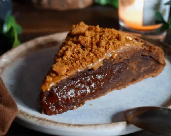 Une part de gâteau speculoos, riche et gourmande, garnie de miettes de biscuits et d'une sauce caramel.