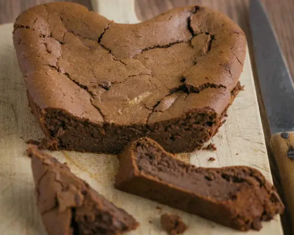 Un délicieux gâteau au chocolat en forme de cœur, un gâteau sans oeuf, craquelé sur le dessus, avec une part coupée.
