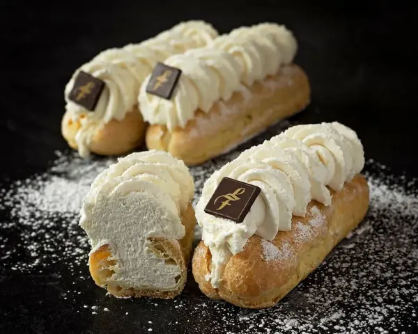 Trois éclairs chantilly généreusement garnis de crème fouettée, ornés d'un carré de chocolat, saupoudrés de sucre glace.