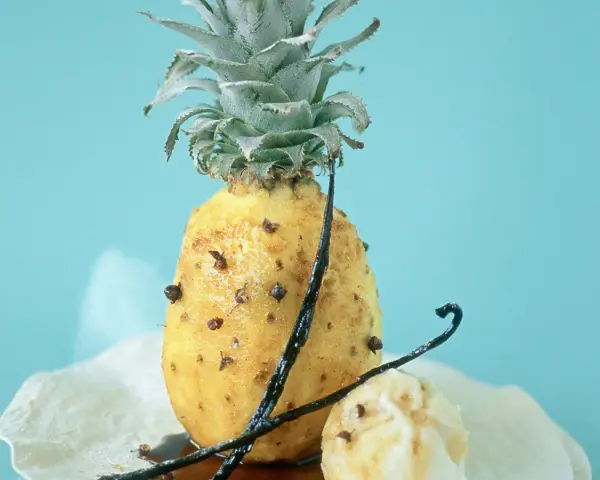 Un ananas rôti, parsemé de clous de girofle et de gousses de vanille, sur un fond bleu pâle. Un délice sucré et épicé.