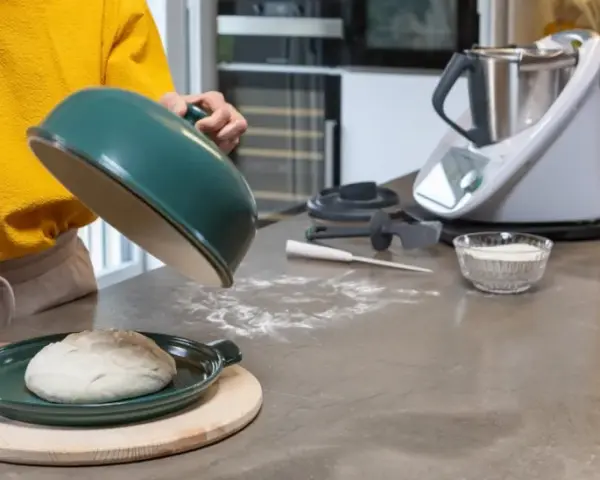 Préparation de la pâte à pizza avec un robot culinaire. Une boule de pâte repose sur un plat vert, prête à être cuite.