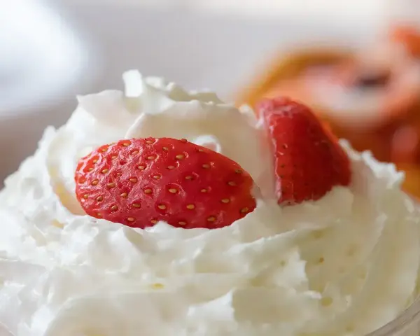 Chantilly aérienne garnie de fraises fraîches. Une invitation à découvrir comment faire de la chantilly maison pour un dessert parfait.
