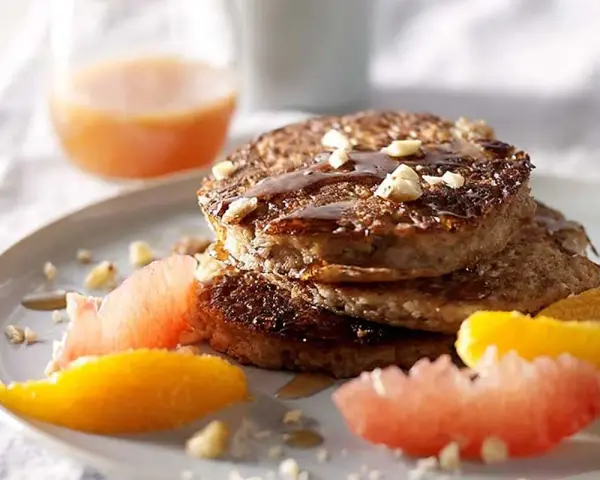 Pile de pancakes muesli, nappés de sirop et garnis de noix, accompagnés de quartiers d'agrumes.