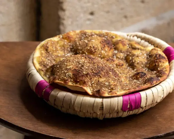 Manouche au zaatar, un délice croustillant aux épices, servi dans un panier tressé aux accents fuchsia.