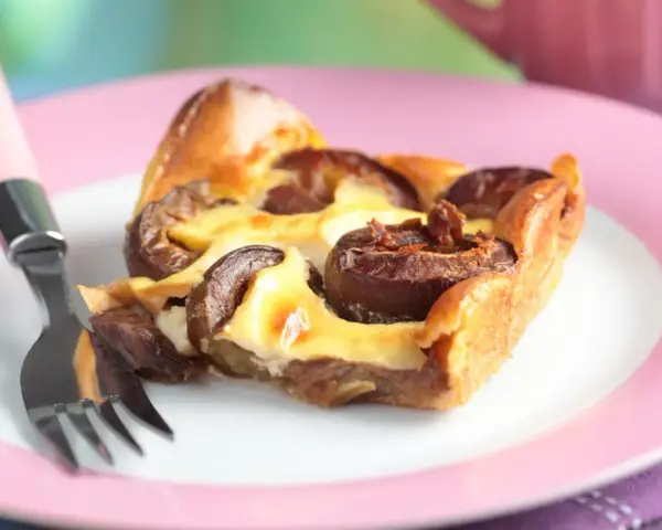 Tranche de clafoutis aux prunes moelleux sur une assiette rose avec une fourchette.