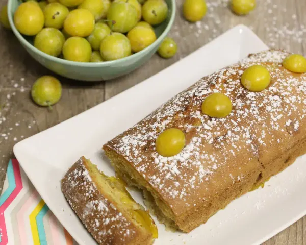 Gâteau lorrain aux mirabelles, saupoudré de sucre glace, avec des mirabelles fraîches sur le dessus et dans une coupelle à côté.
