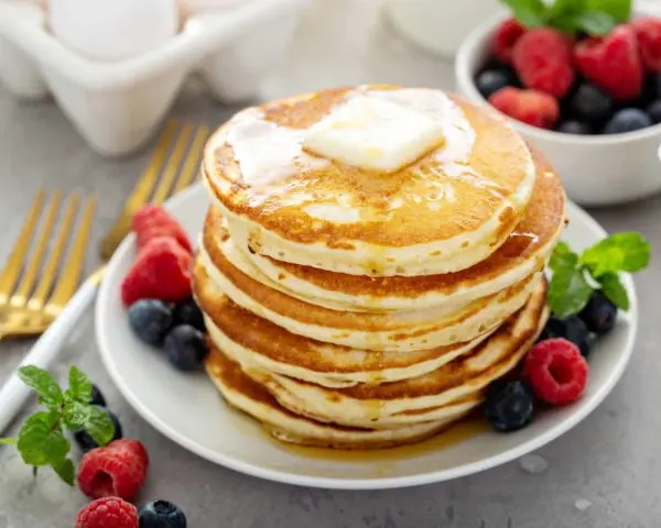 Pile de pancakes sans oeuf, dorés et moelleux, garnis de beurre fondant et de fruits rouges frais. Un délice pour le petit-déjeuner !