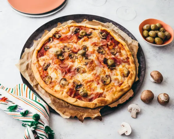 Une délicieuse pizza reine, garnie de jambon, champignons et olives, prête à être dégustée.