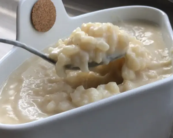Cuillère prélevant une portion crémeuse de riz au lait dans un bol blanc.