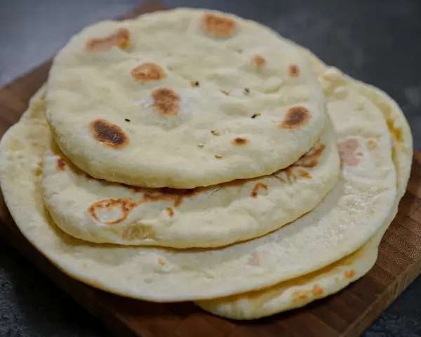 Pile de pains arabes moelleux, légèrement dorés par la cuisson, sur une planche en bois. Parfait pour accompagner un repas.
