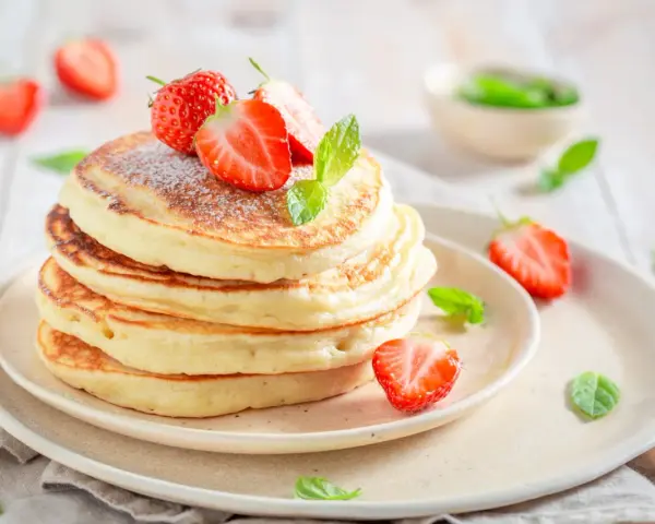 Pile de pancakes moelleux, décorés de fraises fraîches et de menthe, comme ceux de Cyril Lignac. Un délice !
