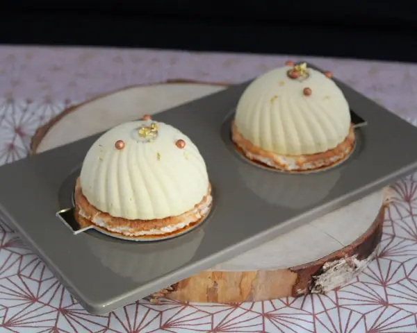 Deux dômes de dessert fruités, ornés de perles cuivrées et de feuilles d'or, reposent sur un plateau gris.