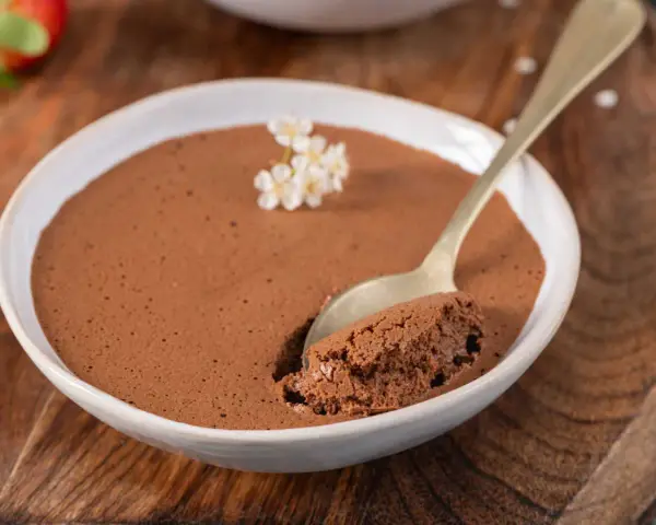 Une cuillère prend une bouchée d'une mousse au chocolat au lait aérienne, décorée de petites fleurs blanches.