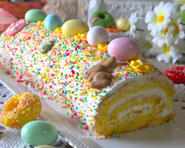 Bûche roulée décorée pour Pâques, recouverte d'un glaçage mascarpone facile et de vermicelles colorés, avec des œufs et un lapin en chocolat.