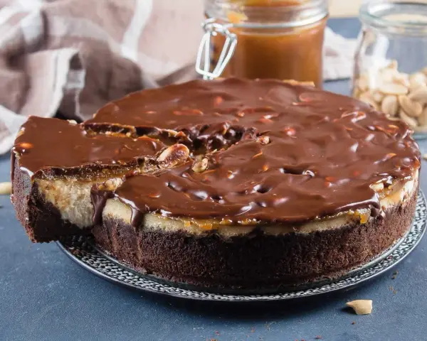 Gâteau façon Snickers, avec une base chocolatée, une couche crémeuse, du caramel coulant et une ganache au chocolat parsemée de cacahuètes. Un délice !