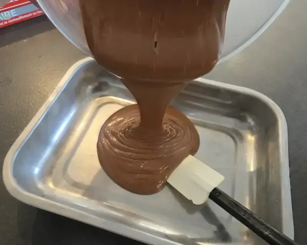 Une ganache au chocolat, inspirée par le Toblerone, est versée dans un plat métallique. Une spatule aide à l'étaler.