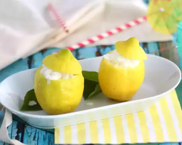 Deux citrons évidés remplis de sorbet citron, servis sur une assiette blanche, avec des feuilles vertes et des pailles colorées en arrière-plan.