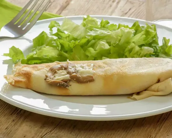 Une ficelle picarde garnie de champignons et de fromage, accompagnée d'une salade verte croquante sur une assiette blanche.