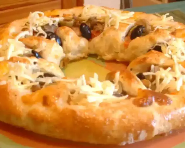 Pizza maison avec une croûte dorée, garnie d'olives noires et de fromage râpé. Parfait pour une recette pâte à pizza rapide.