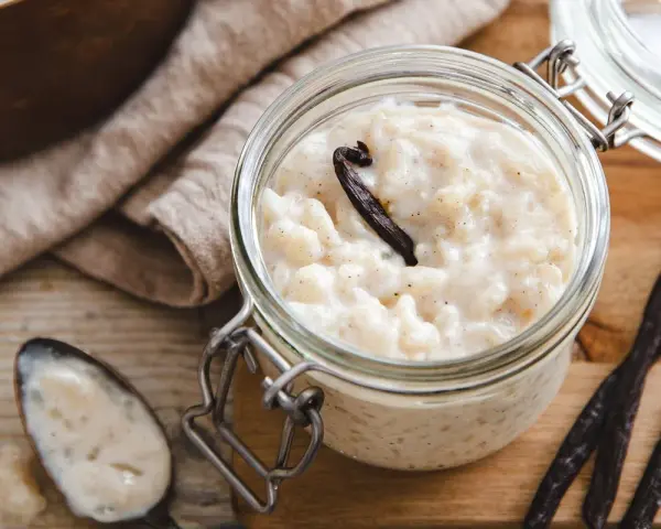 Un pot en verre rempli de riz au lait au four, garni d'une gousse de vanille. Une cuillère à côté en témoigne.