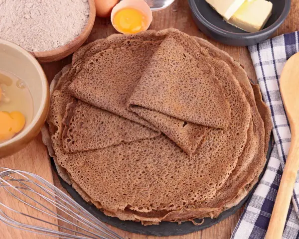 Pile de crêpes de sarrasin, avec des ingrédients pour la pâte à crêpe sarrasin : farine, œufs, beurre.