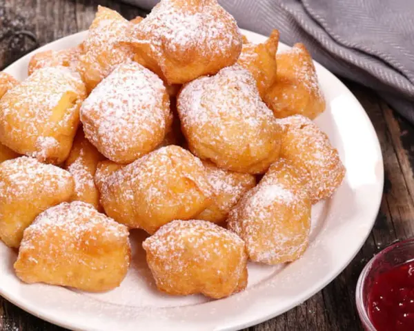 Une assiette de beignets banane saupoudrés de sucre glace, prêts à être dégustés avec une confiture de fruits rouges.
