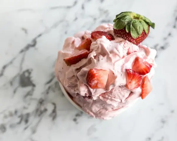 Un délice rose et crémeux : un sorbet fraise garni de morceaux de fruits frais et d'une fraise entière sur un fond marbré.