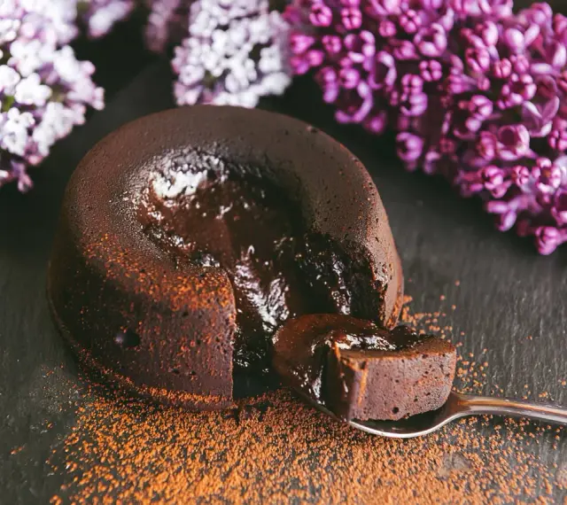 Un fondant au chocolat coulant, saupoudré de cacao, avec des fleurs de lilas en arrière-plan. Une bouchée parfaite.
