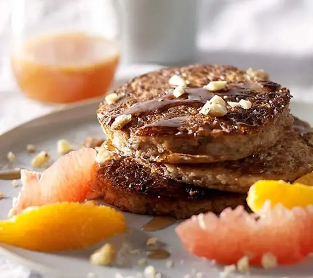 Pile de pancakes muesli, nappés de sirop et garnis de noix, accompagnés de quartiers d'agrumes.