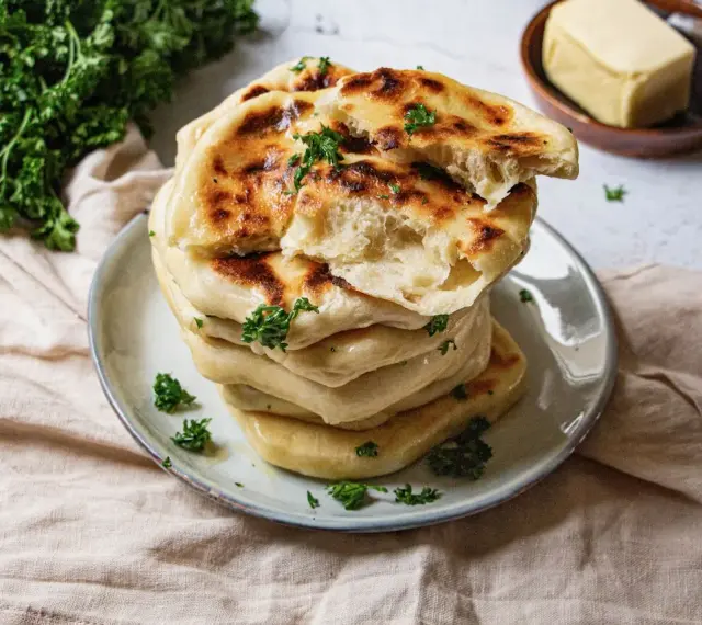 Pile de cheese naan moelleux, dorés et parsemés de persil frais. Un délice à déguster avec du beurre.