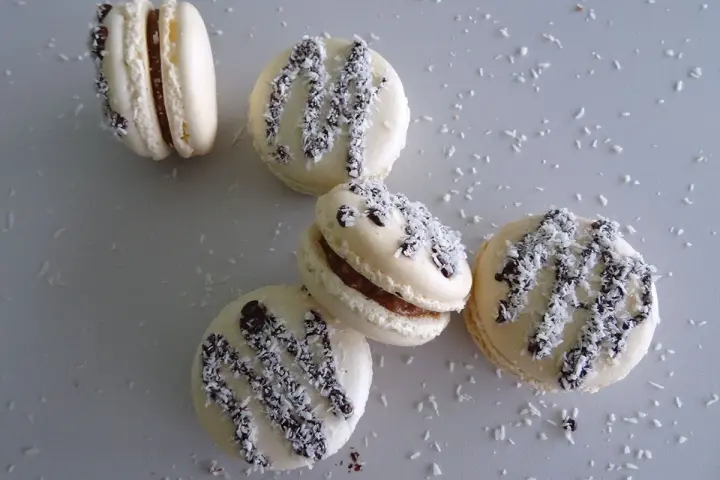 Macarons à la ganache coco, parsemés de noix de coco râpée et de copeaux de chocolat noir.