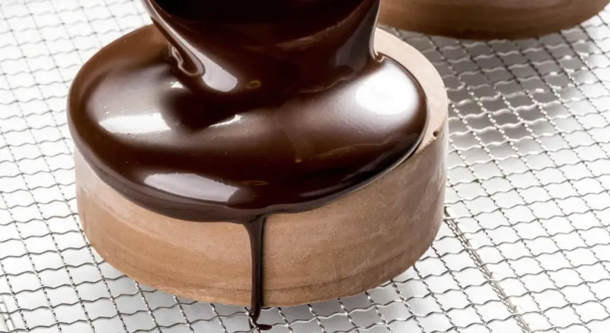 Un glaçage chocolat brillant et onctueux recouvre un petit gâteau rond, coulant sur les côtés.