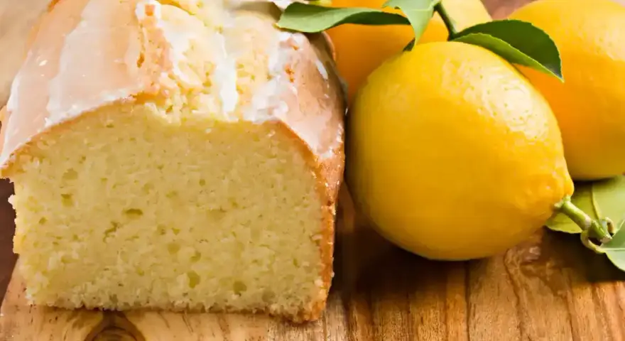 Un délicieux gâteau citron, avec un glaçage blanc et des citrons frais sur une planche en bois.