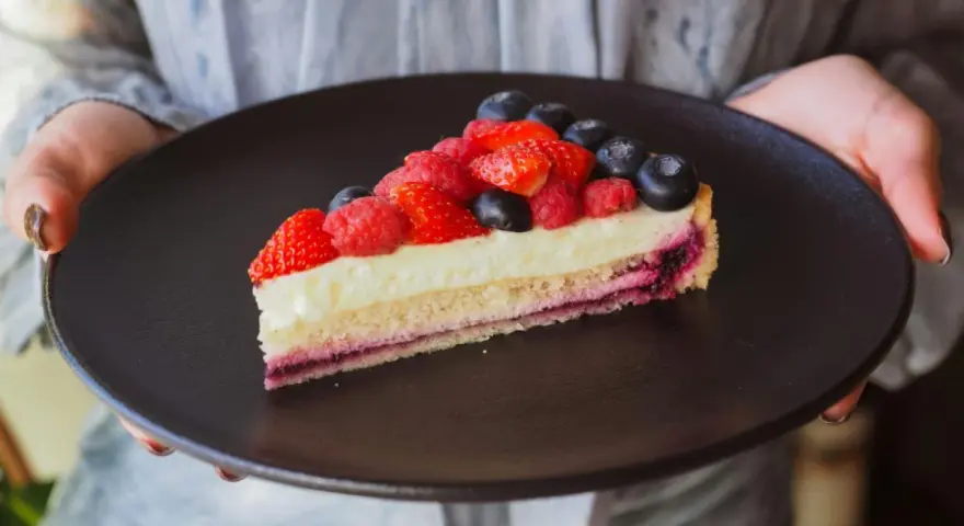 Tranche de tarte aux fruits rouges sur une crème mousseline onctueuse, présentée sur une assiette noire.