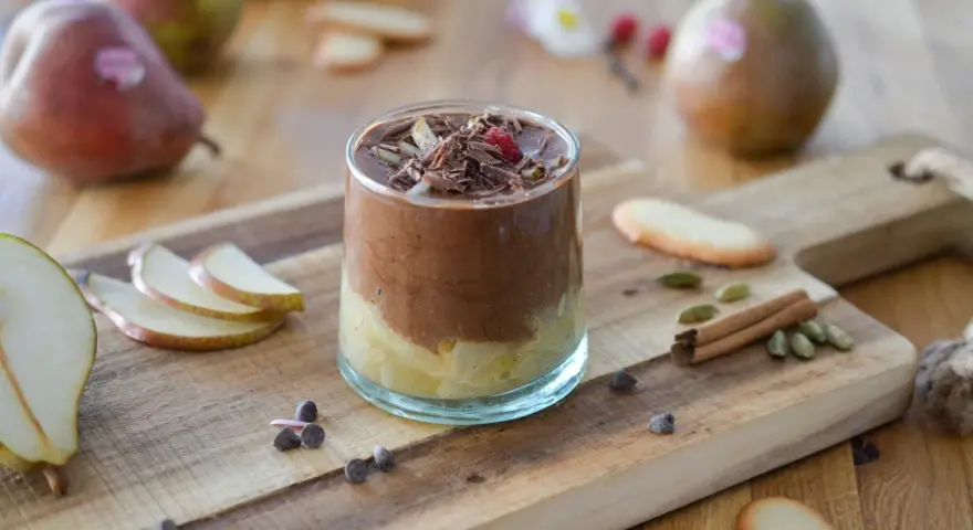 Délicieuse recette mousse poire chocolat, garnie de copeaux de chocolat et d'une framboise. Poires fraîches et épices sur fond de bois.