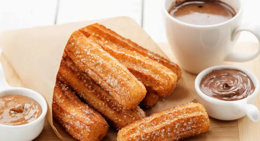 Churros dorés et croustillants, saupoudrés de sucre, prêts à être trempés dans le chocolat. Une recette gourmande pour un goûter parfait.