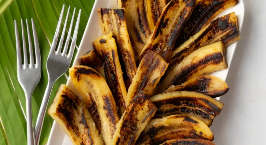 Bananes flambées grillées sur une feuille de bananier, prêtes à être dégustées avec deux fourchettes.