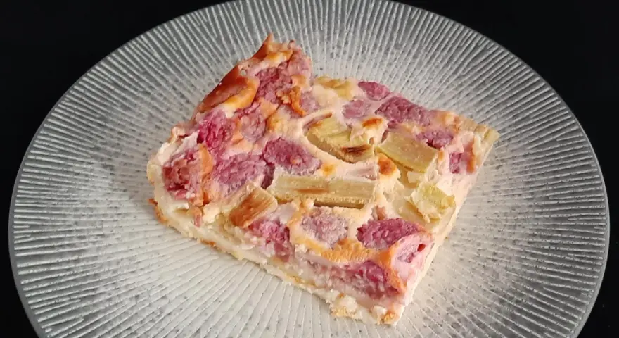 Tranche de clafoutis rhubarbe aux fruits rouges, sur une assiette transparente aux motifs rayonnants.