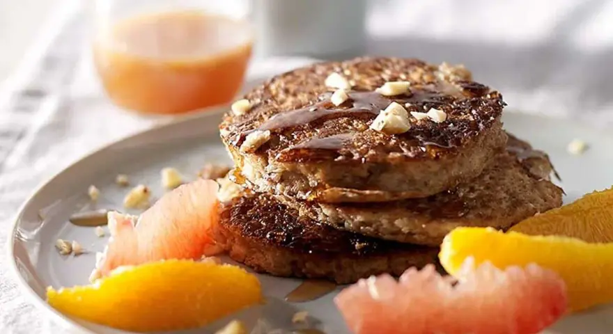 Pile de pancakes muesli, nappés de sirop et garnis de noix, accompagnés de quartiers d'agrumes.