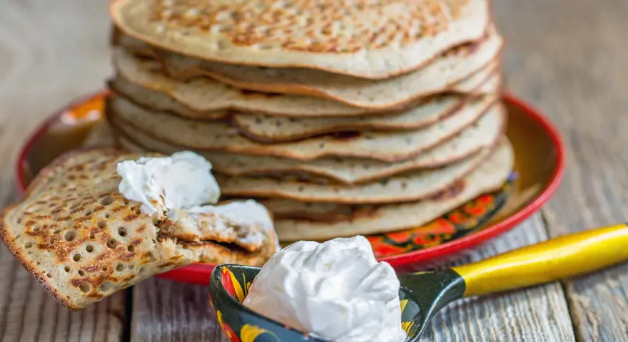 Pile de crêpes épaisses alsaciennes, garnies de crème fraîche. Une cuillère décorée en est aussi remplie.