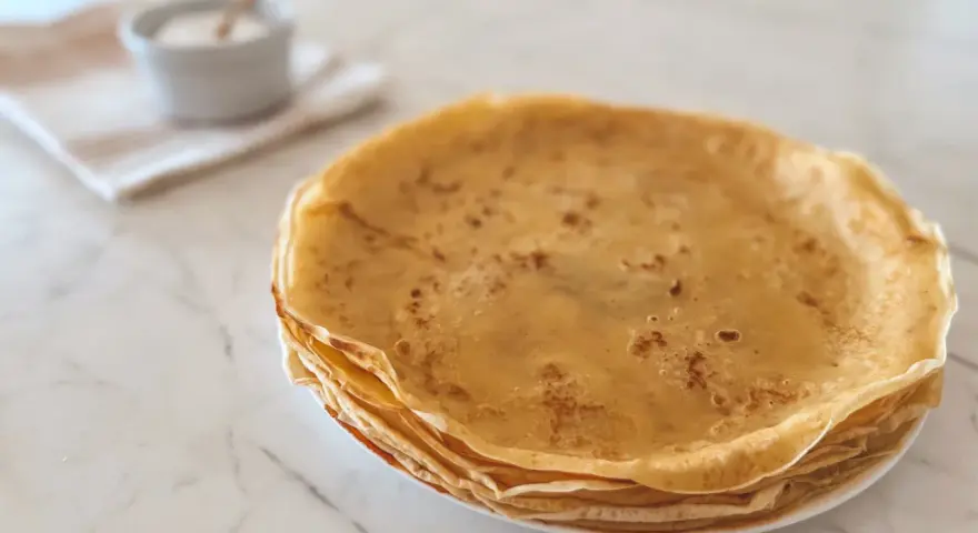 Pile de crêpes dorées, parfaites pour une recette crêpe moelleuse. Un petit bol de sucre est à côté.