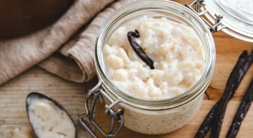 Un pot en verre rempli de riz au lait au four, garni d'une gousse de vanille. Une cuillère à côté en témoigne.